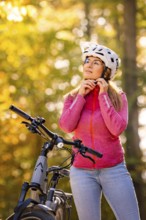 Woman opens helmet on ebike through the autumn forest, Black Forest, Gechingen, Germany, Europe