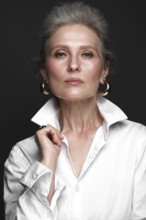 Portrait of a beautiful elderly woman in a white shirt with classic makeup and gray hair