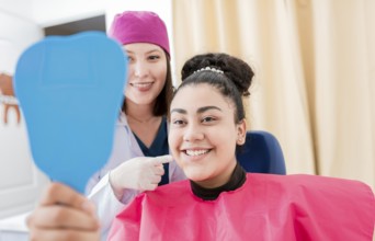 Satisfied patient in dental clinic looking at mirror, dentist next to satisfied patient smiling at