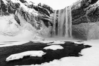 Skogafoss waterfall with icy and snowy rock face, black and white photo, Sudurland, Iceland, Europe