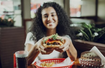 Happy girl showing burger in a restaurant. Close-up of a girl showing appetizing hamburger in a