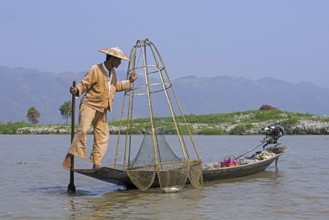 Intha fisherman steering traditional fishing boat by wrapping his leg around the oar, Inle Lake,