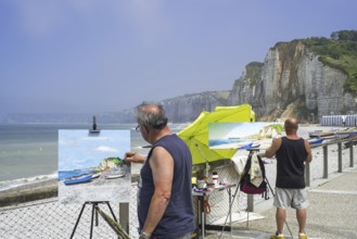 Landscape painters painting fishing boats, caïques on beach and sea cliffs at seaside resort Yport,