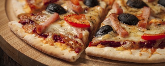 Letterbox panorama of sliced ham pizza with (capsicum) and olives on wooden board on table