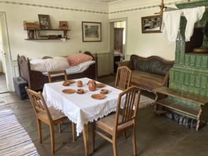 Room with dining table simple earthenware dishes four chairs bed leather sofa tiled stove in