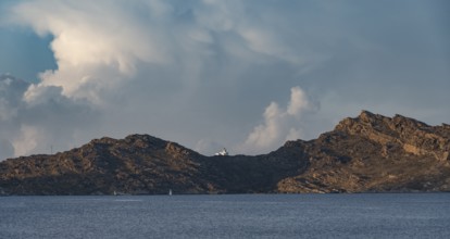 Rocky coast with lighthouse Akrotiri Korakas with blue sea, dramatic cloudy sky Paros, Cyclades