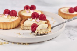 Piece of small tartlet pastry with white cream, topped with raspberry fruits and almond sprinkles