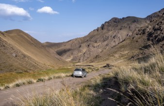 Off-road vehicle at the mountain pass at Songköl, gravel road at a plateau, mountains behind,