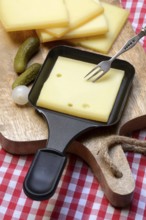 Raclette, cheese slices on wooden board and in raclette pans, Switzerland, Europe