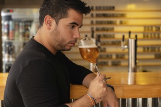 Close-up of a young Latino man savoring a beer in a nightclub. His serious expression and