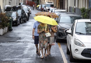 People with umbrellas walk through a street in Diana Marina, Italy, 18/08/2024, Diano Marina,