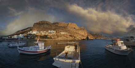 Boats in the harbour of the fishing village of Finiki against a rocky backdrop with evening clouds,