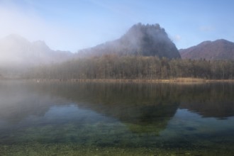 Lake Almsee in autumn with the mountain Ameisstein behind. The fog is lifting