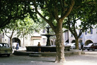 Little boy playing at the fountain in the shade of the trees in the city centre of Uzès, France,