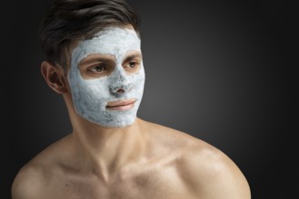 Portrait of a beautiful, relaxed young man with a face mask made of clay, skin care for face and