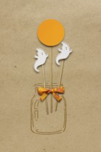 Creative Halloween concept photo of a bottle with ghosts made of paper on a brown background