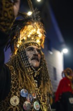 Man in festive, feathery costume with illuminated hat and decorated buttons at night event,