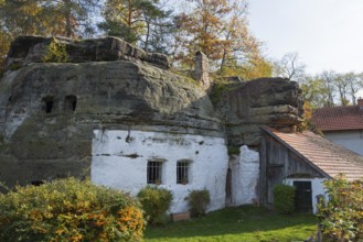 A house built into a rock, surrounded by autumn trees under a blue sky, rock dwelling, museum,