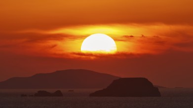 Sun setting over the sea with islands on the horizon, sky in intense orange tones, sunset, Kassos,