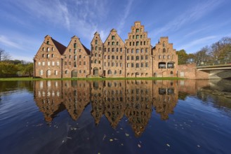 Historic salt warehouses with reflections on the water surface of the Trave, blue sky with veil