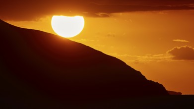 Sinking sun behind a mountain slope, intense orange light in the sky, sunset, Kassos, Karpathos,