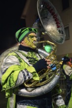 Musician in striking green costume plays a trumpet at a night-time event, carnival, Tiefenbronn,