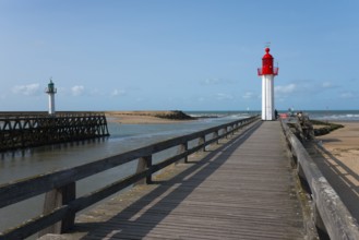 Red and green lighthouses along a wooden walkway on the coast under a blue sky, green lighthouse in