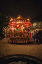 An illuminated carousel at a Christmas market surrounded by half-timbered houses at night,