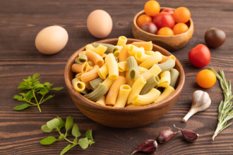 Rigatoni colored raw pasta with tomato, eggs, spices, herbs on brown wooden background. Side view,