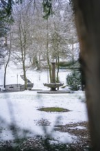 Snow-covered park landscape with a central fountain and surrounding trees, spa garden, Bad Wildbad,