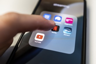 One finger touches the Netflix app icon on a smartphone screen with various other streaming apps