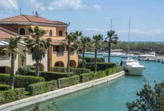 Leisure boats at quay in canal and with palm trees and holiday homes in Lido di Policoro resort,