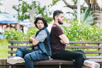 Two angry friends sitting on a park bench. Two friends arguing on a park bench