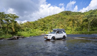 Toyota off-road vehicle with roof tent drives through a wide river in the rainforest, Alajuela