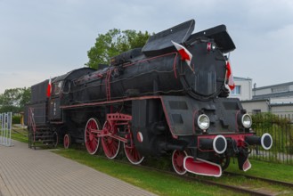 Front view of a black steam locomotive with red details in an open-air museum, Polish steam