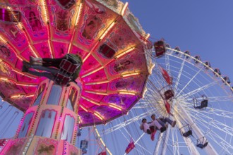 Illuminated chain carousel and Ferris wheel at night with cheerful people, funfair, wave flight,