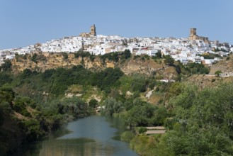 Whitewashed houses on a green hill along a river under a clear sky, Arcos de la Frontera, Guadalete