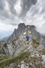 Mountaineer with helmet on a narrow hiking trail on a rocky ridge, ascent to the Maukspitze, clouds