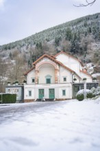 A snow-covered theatre building against a wooded mountain backdrop in winter, Königliches