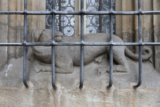 Dog sculpture behind the iron grating of a pointed arch window at the late Gothic hall church of St