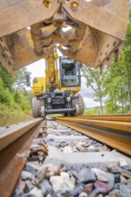 Excavator with shovel on railway tracks in a green environment, track construction, Hermann