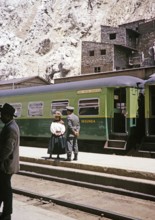 Indigenous woman and railway official standing on the platform at the train, La Oroya railway