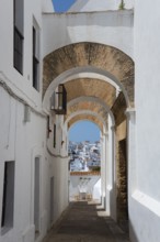 Narrow passageway with arches and white facades in a Mediterranean town in the sunshine, view