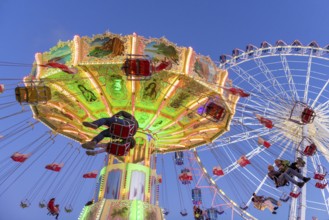 Illuminated chain carousel and Ferris wheel at night with cheerful people, funfair, wave flight,