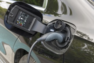 Electric car being charged at charging station, charging cable plugged into black vehicle,