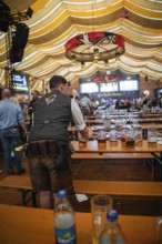 A waiter collects beer mugs from the tables in the marquee, Canstatter Wasen, Stuttgart, Germany,