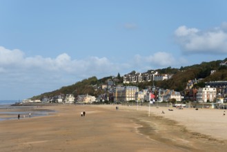 A wide sandy beach with few people, lined by a coastal town under a clear sky, Trouville-sur-Mer,