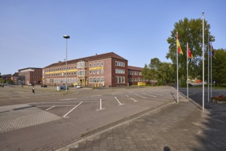 Former post office, lantern, flagpoles, car park with parking boxes, trees, blue cloudless sky,