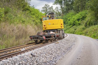 Yellow construction machine on a railway track next to a road in a green environment, track