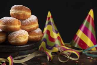 Piles of doughnuts with colourful paper streamers, confetti and party hats on a dark table,